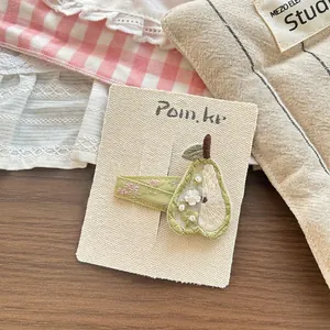 Close-up of handmade embroidered pear hair clip with delicate green beads and floral ribbon