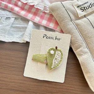 Detailed view of hand-knitted leaf hair clip with white pearls on a textured card