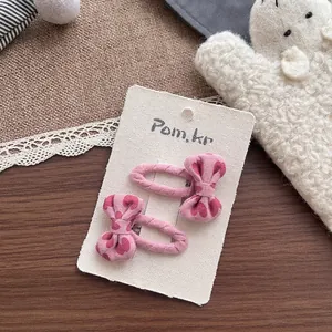 Vue détaillée des barrettes à nœud rose avec motifs de cœurs sur carte de support
