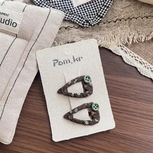 Macro detail of brown floral fabric hair clip with green button on display card