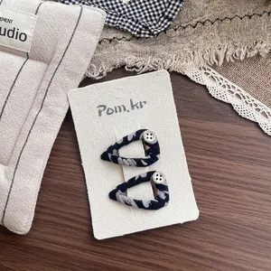 Close-up of fabric-wrapped BB hair clips with vintage buttons on a white textured card