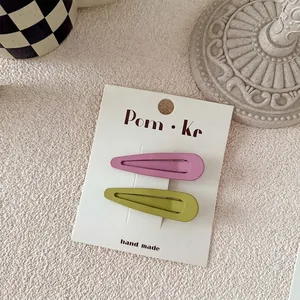 Detailed macro view of pink and olive green matte metal BB hair clips on brand card