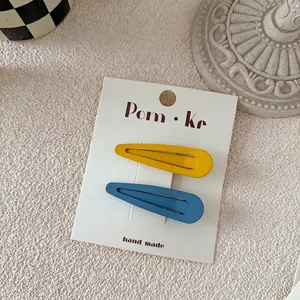 Detail of matte waterdrop hair clips in yellow and blue on white card packaging