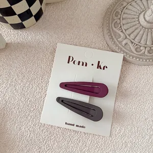 Close-up of matte teardrop hair clips in purple and dark gray on display card