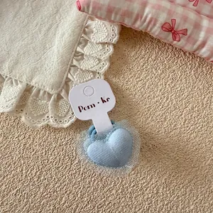 Détail d'un chouchou cœur bleu en peluche avec bordure en dentelle sur support blanc