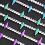 Macro detail of iced-out chains with blue green and purple spike pendants on dark background
