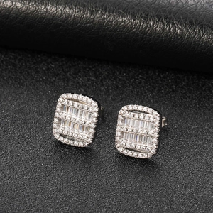Macro detail of square zircon stud earrings with baguette-cut stones on black leather background