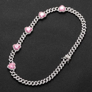 Detailed macro view of silver Cuban link chain with pink heart zircons on black background
