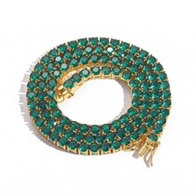 Detailed close-up of a gold-plated tennis bracelet with round green cubic zirconia stones