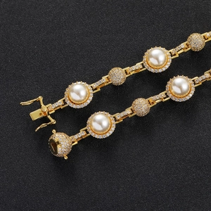 Close-up of hip hop gold bracelet featuring pavé crystals and white pearls on black background