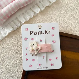 Detalle de horquilla rosa con gato bordado blanco sobre base de encaje floral