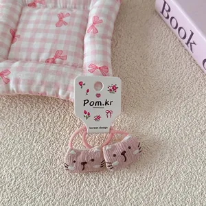 Detail van roze kattenhaarelastiekjes op witte kaart over een gezellige ruitjesachtergrond