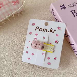 Detail van een roze gestreepte kattenhaarclip met geel kant op een displaykaartje