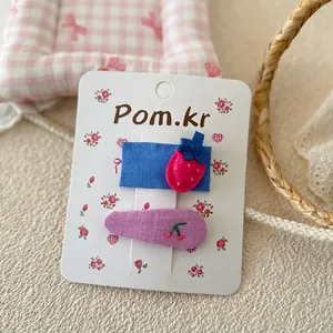 Détail de barrettes en tissu brodé avec motifs fraises et cerises sur carte fleurie