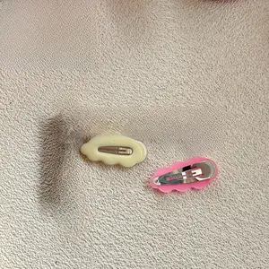 Close-up of wavy cloud-shaped hair clips in cream and pink with metal BB clips