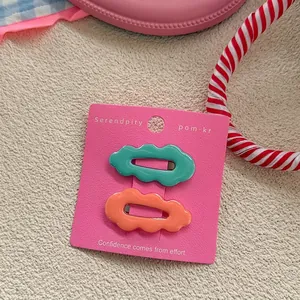 Detail view of wavy hair clips in mint green and coral orange on pink display card