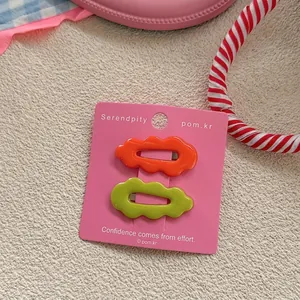 Detail of candy-colored wavy hair clips in orange and lime green on pink card