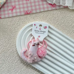 Close-up of pink cat-shaped hair tie with floral embroidery and soft pom-pom detail