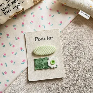 Détail de pinces à cheveux BB à carreaux verts et set floral en dentelle sur carte
