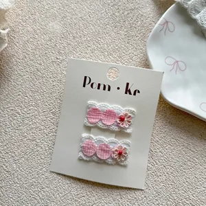 Detail of pink plaid hair clips with white lace trim and tiny floral accents on card