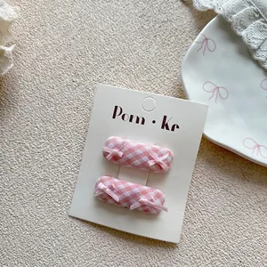 Close-up of handmade pink plaid hair clips with tiny ribbon bows on a display card