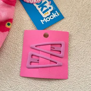 Détail de barrettes triangulaires rose mat sur une carte de présentation rose pastel