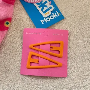 Détail de barrettes triangles orange mat sur carte rose pour la coiffure