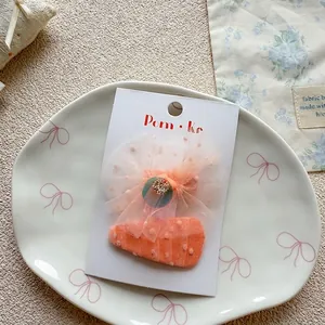 Close-up of orange-pink tulle bow and triangle hair clips with sequins on a display card
