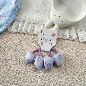 Detail of purple satin bow hair ties with pearl accents and floral embroidery on white card