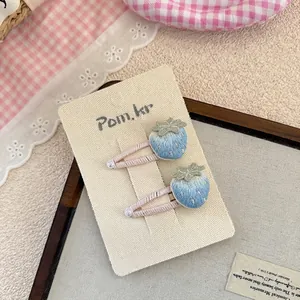Nahaufnahme von blauen Erdbeer-Haarspangen mit feiner Stickerei, Perlen und rosa Band