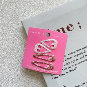 Detailed view of four glittery heart and water drop hair clips on a pink display card