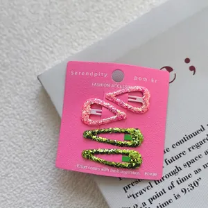 Close-up of four glittery pink and green hair clips for girls on a pink card base