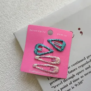 Detail view of four sparkling sequin heart and teardrop hair clips on pink card