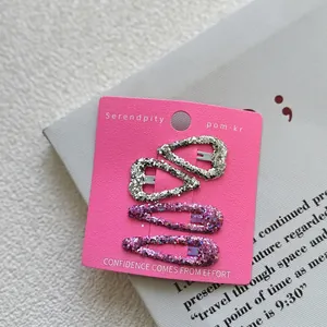 Close-up of four glittery silver and purple sequin hair clips on pink display card
