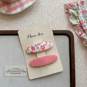 Lot de barrettes à fleurs et tissu rose sur carte de présentation et fond doux pastel