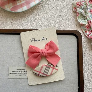 Détail d'un nœud rose et de barrettes à carreaux beige sur une carte support