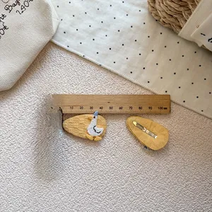Dettaglio di due fermagli per capelli in peluche giallo con ricamo a forma di papera