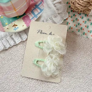 Detail of two white organza flower hair clips with green grosgrain ribbon wrapping