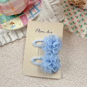 Detailed view of two blue chiffon flower hair clips on a cream-colored card holder