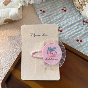 Close-up of pink cherry embroidery hair clip with white lace trim on a card