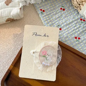 Detail of cute white embroidered bunny hair clip with pearls on a product display card