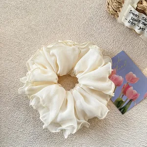 Detail of a large cream-colored chiffon hair scrunchie with layered ruffle texture