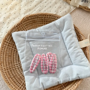 Détail de quatre barrettes BB à carreaux roses dans une pochette zippée sur tissu bleu doux