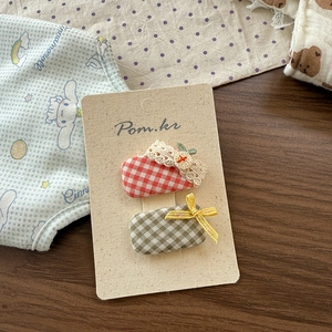 Detail view of red lace and green plaid bow hair clips on a display card for girls