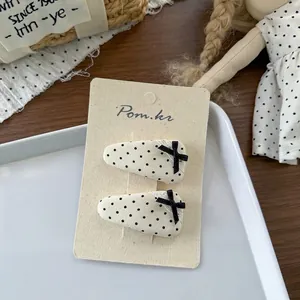 Detailweergave van twee crèmekleurige haarspeldjes met stippen en zwarte strikjes