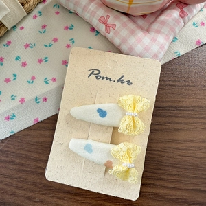 Detail of cream fabric hair clips with blue hearts and yellow lace bows on paper card