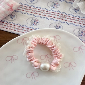 Detailansicht eines rosa Spitzen-Haargummis mit großer Perle auf einem weißen Keramikteller