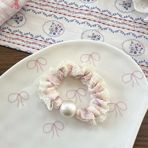Detail eines geblümten Haarscrunchies mit Spitze und weißer Perle auf einem Teller
