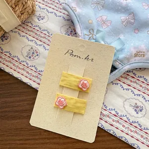 Détail de pinces à cheveux en tissu jaune avec décorations de chatons roses sur carton
