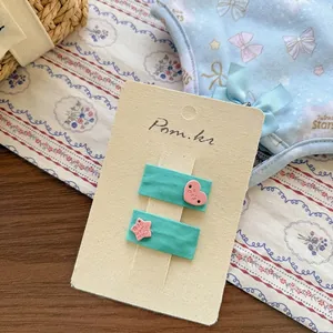 Détail de barrettes en tissu vert avec breloques cœur et étoile roses sur carte support